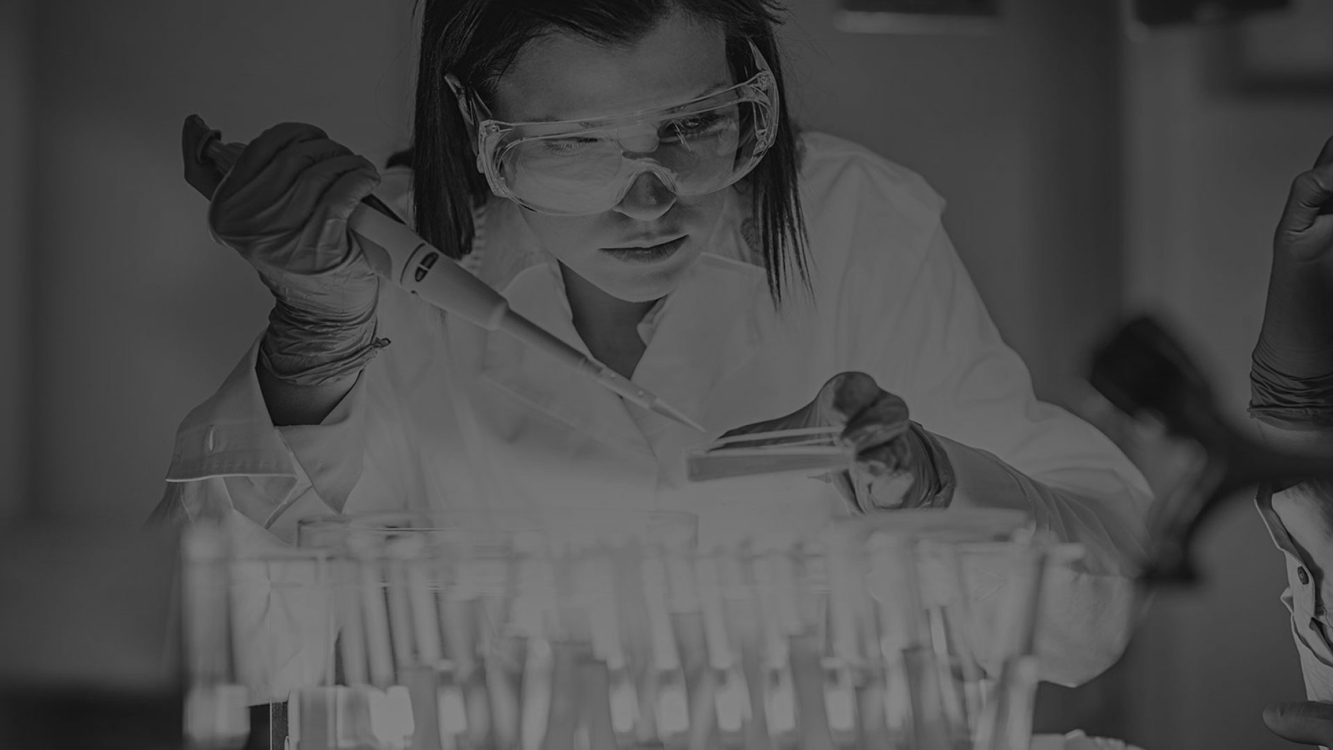 Woman wearing lab coat and safety goggles working with test tubes