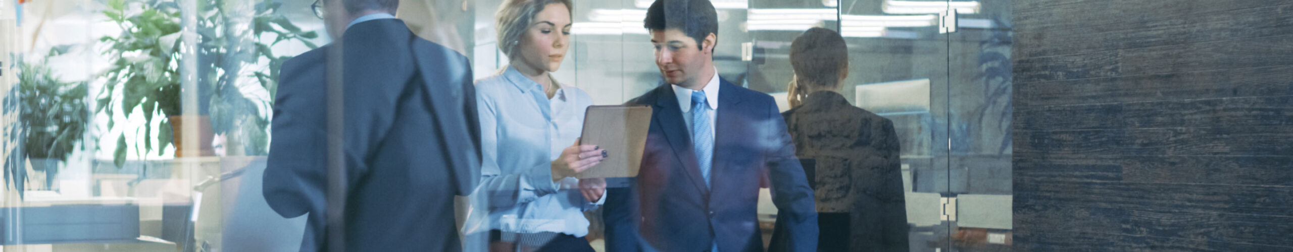 Male and female colleague walking in hall reviewing laptop screen