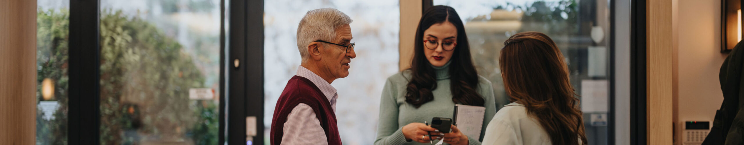 An older male employee standing with two female coworkers in an office setting