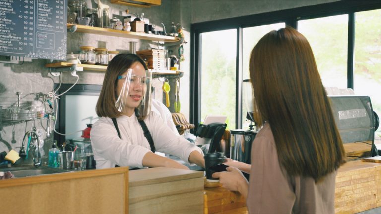 barista wearing COVID-19 face shield and serving coffee to customer