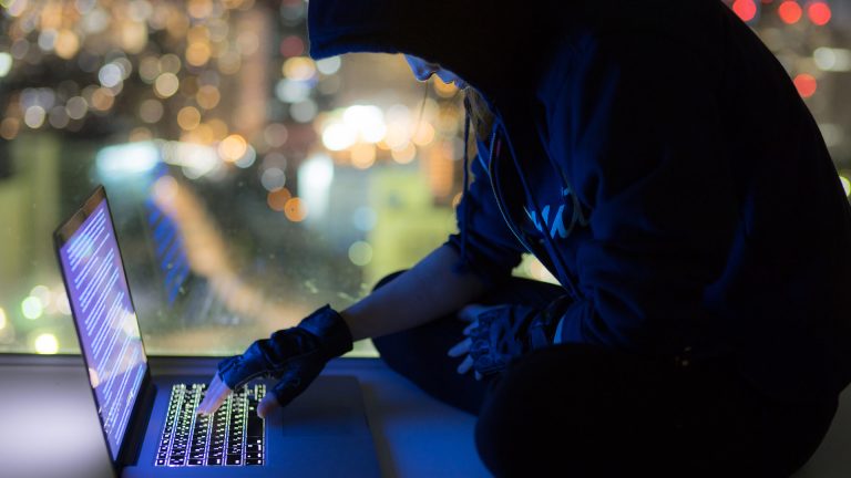 Computer hacker in black hoodie on computer