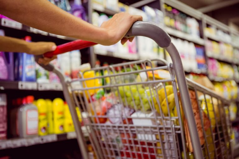 consumer pushing shopping cart through packaged food aisle in grocery store