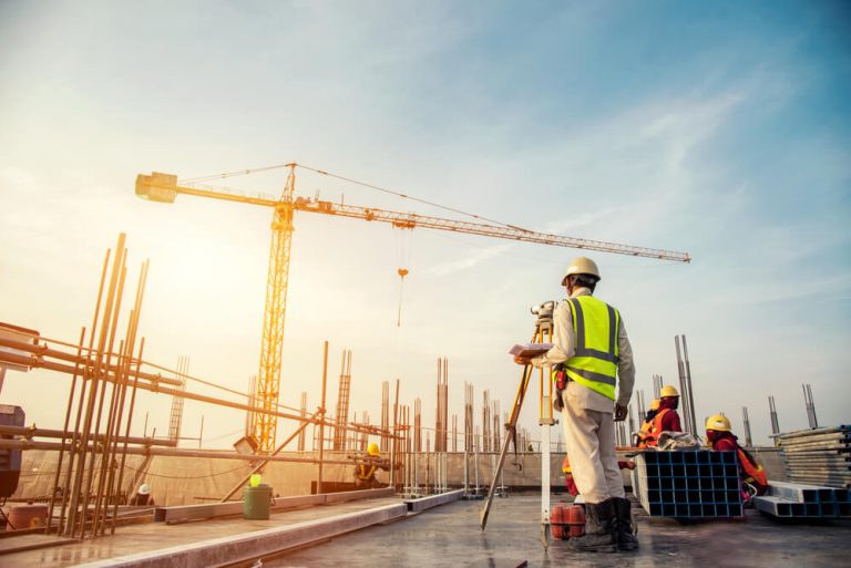 Construction surveyor on site with crane and building progress in background