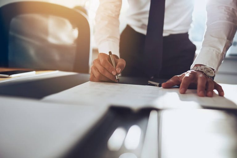 close up of man in suit signing paper on office table