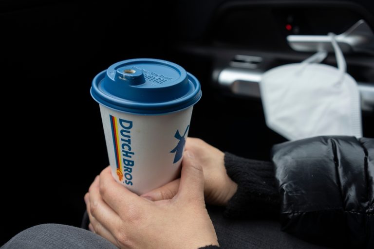 man holding a Dutch Bros coffee cup in a car