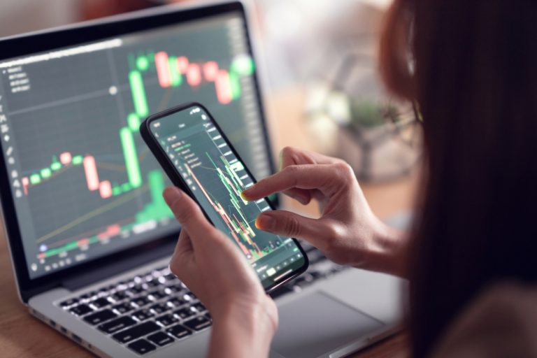 woman checking price on stocks on mobile phone and laptop computer