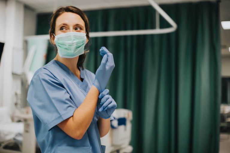 Nurse wearing surgical mask and scrubs in hospital room putting on gloves