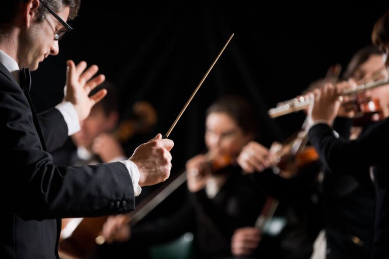 Close up on orchestra conductor with orchestra musicians in background