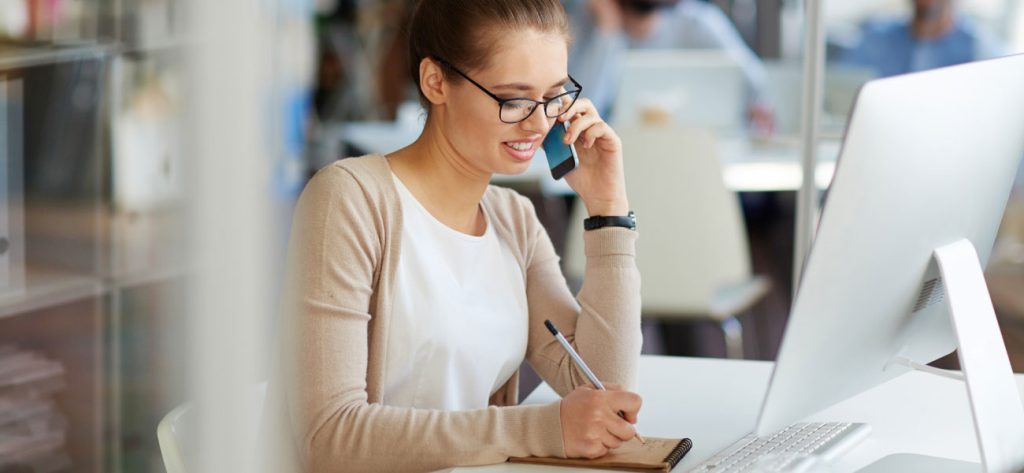 Woman wearing glasses talking on mobile phone while taking notes on notepad