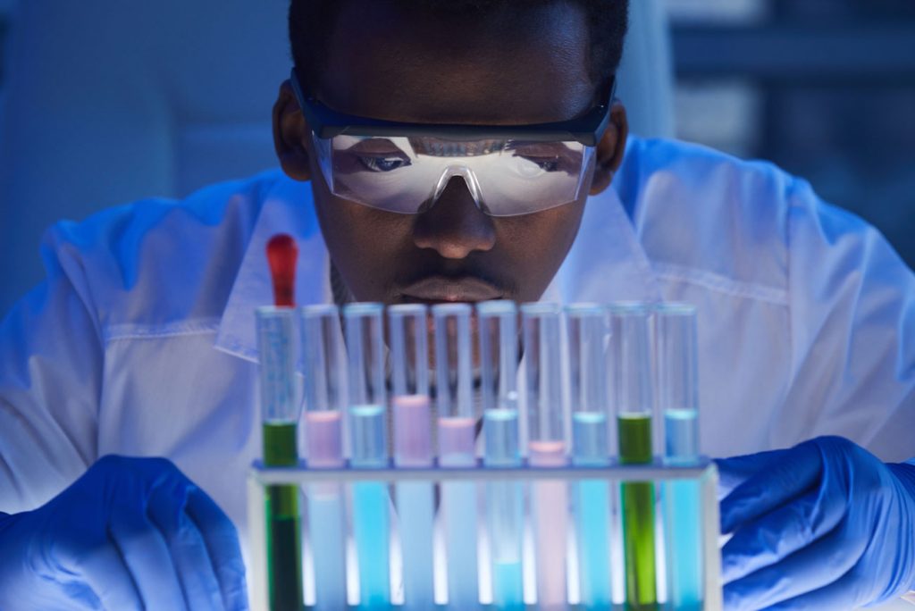 Man wearing safety googles looking closely at test tubes