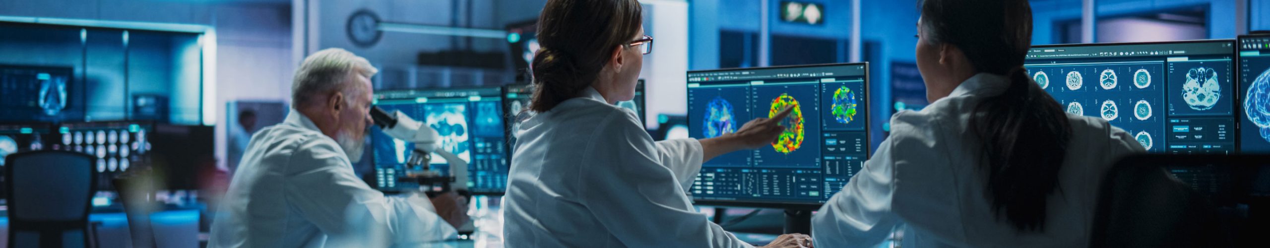 Three physicians working in a lab looking at detailed scans on computer monitors