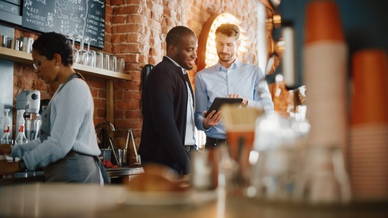 Restaurant owner and host looking at tablet together in kitchen