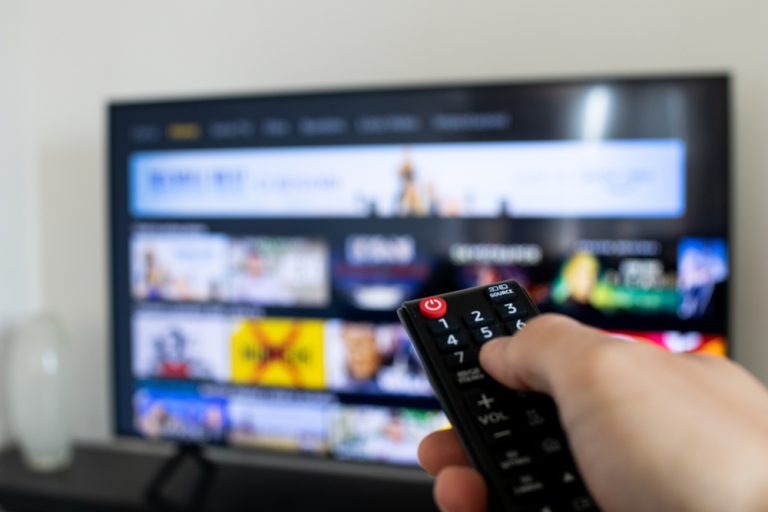 close up of person holding TV remote with streaming platform in the background