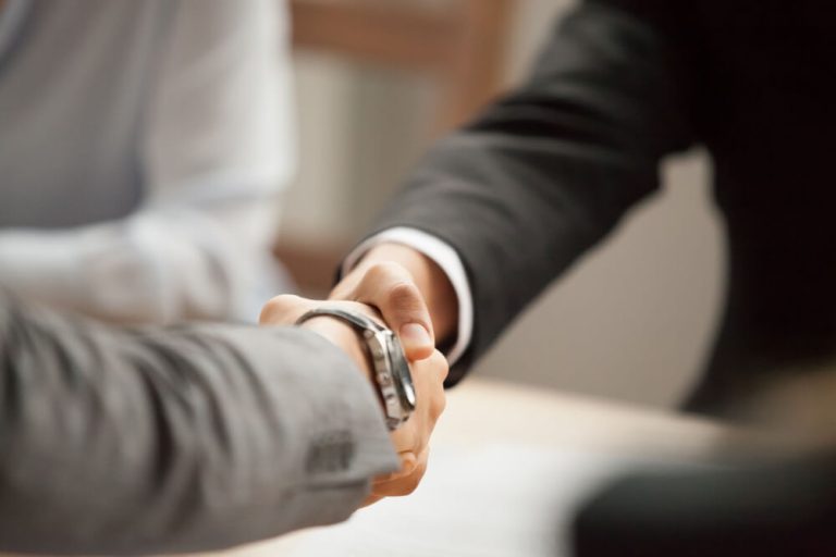 Businessmen shaking hands sealing deal across meeting room table close up