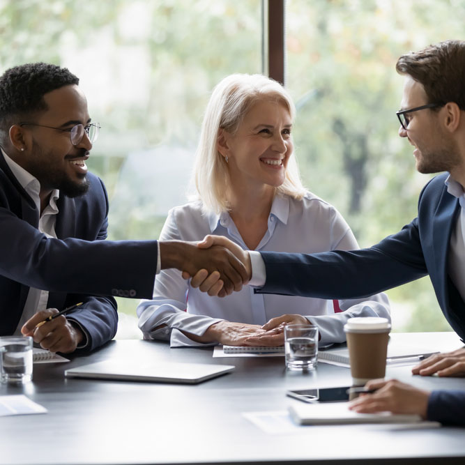 Smiling diverse businesspeople shake hands get acquainted greeting at team meeting in office. Happy multiracial male colleagues employees handshake at briefing with coworkers. Acquaintance concept.