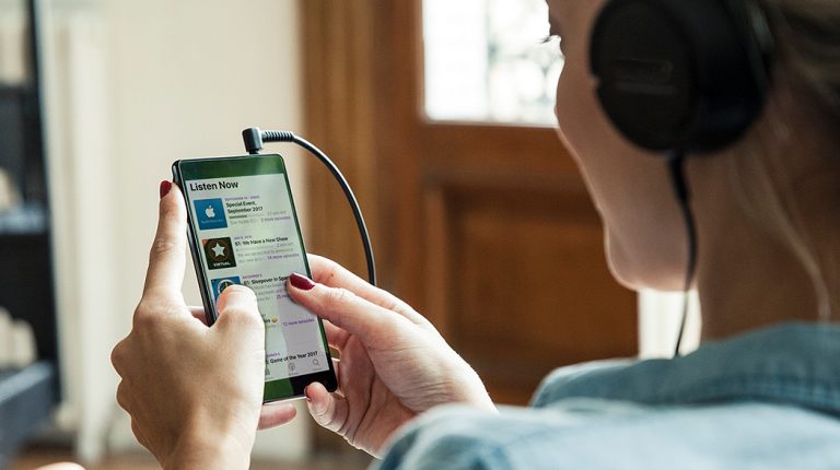 woman with headphones on srolling through list of podcasts on her mobile phone