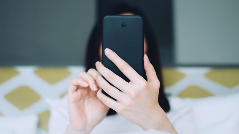 woman in bed holding mobile phone in front of her face