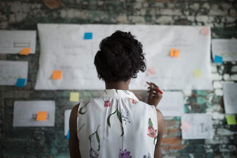 woman holding a pen and facing a wall with plans and sticky notes