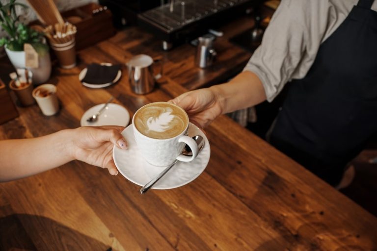 person receiving coffee cup in small cap coffee shop