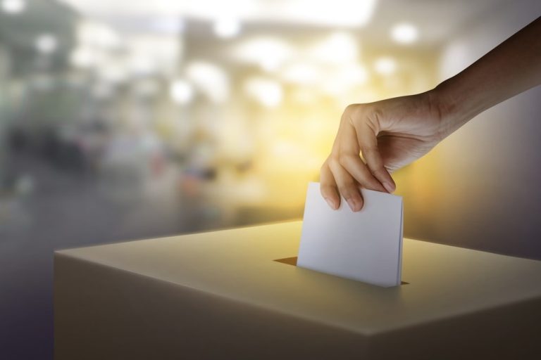 hand dropping ballot into box representing proxy vote and stewardship